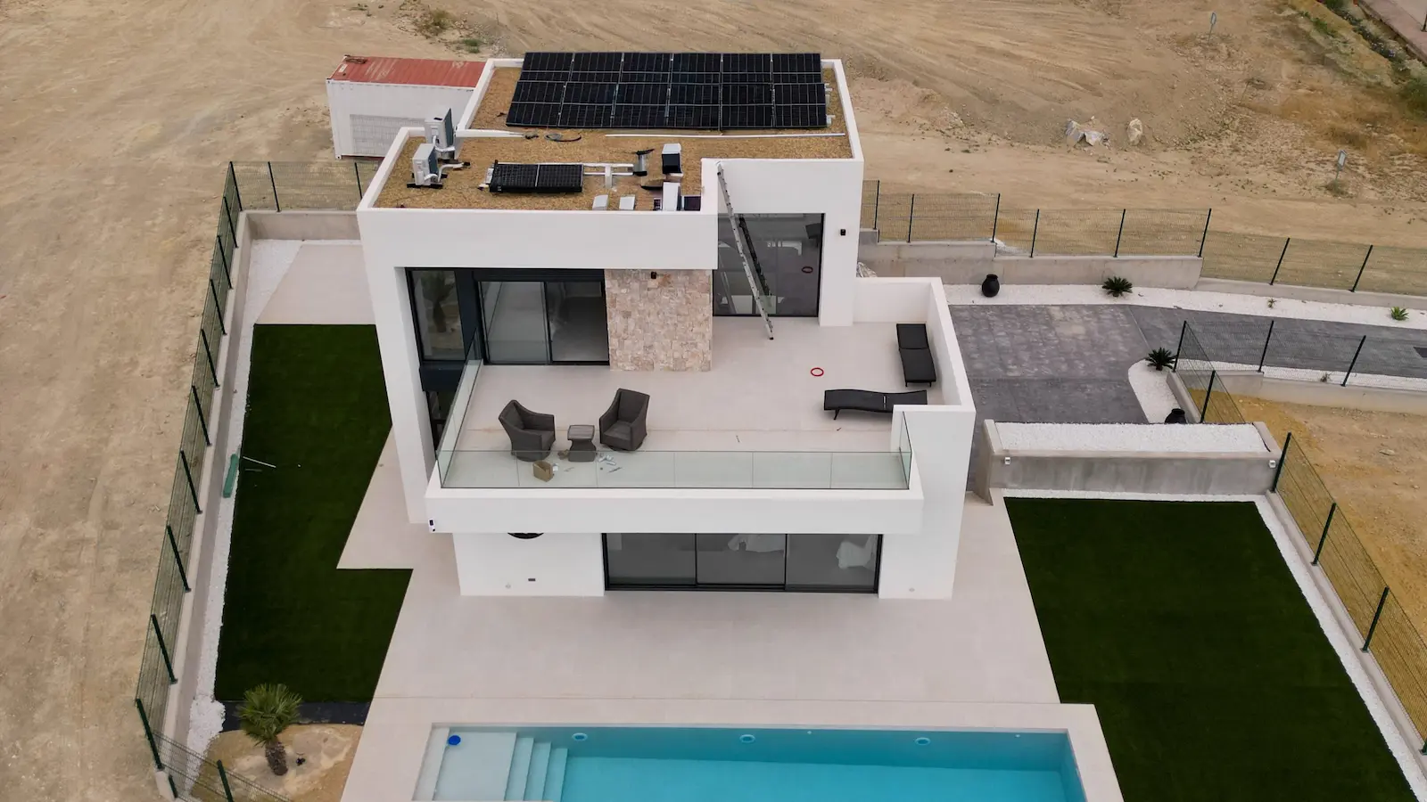 Solar panels installed on the flat roof of a modern white villa with a pool in the foreground